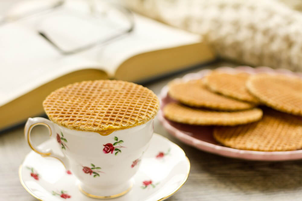stroopwafel on a teacup and several stroopwafels on a plate with an open book in the background