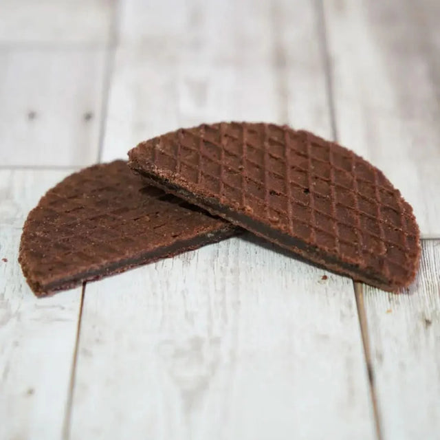 Two cocoa stroopwafels showcasing their textured, chocolatey exterior on a rustic wooden surface.